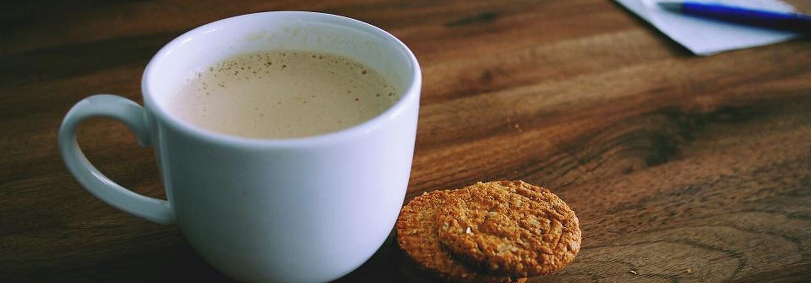 Una taza de café con una galleta al lado sobre una mesa de madera